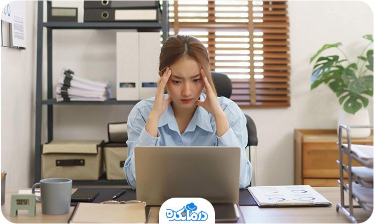 تصویر فردی که پشت میز کار سرش را بین دست‌هایش قرار داده