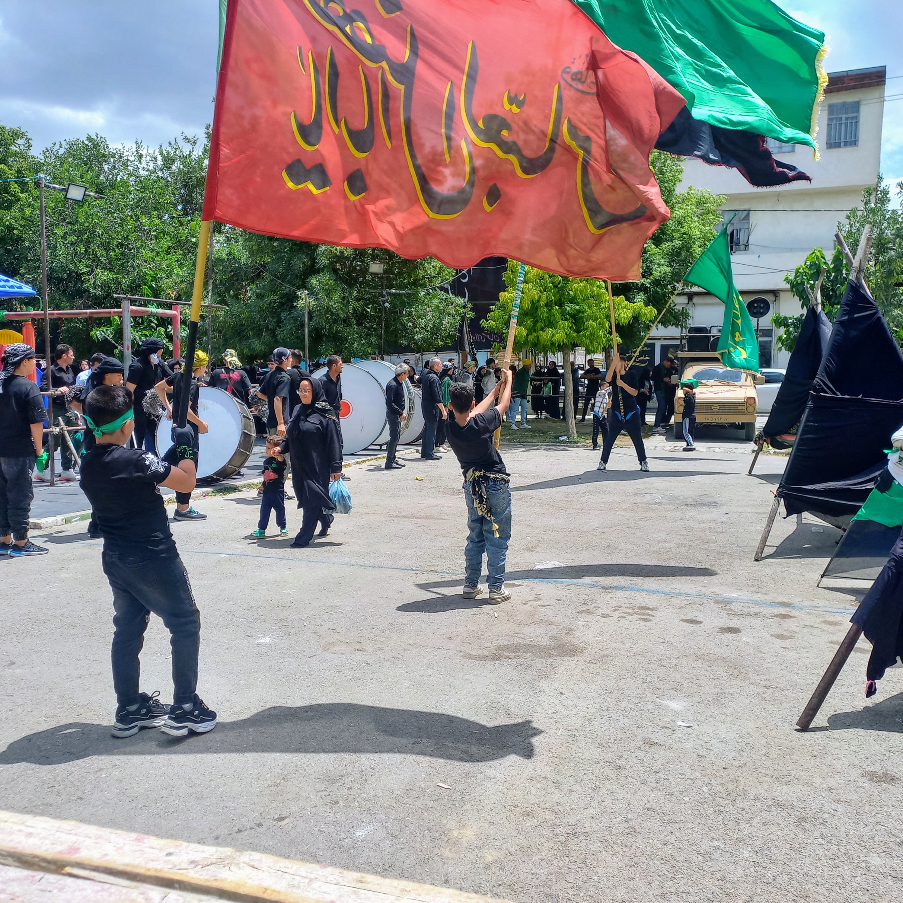 پرچم سرخ «یا  ابالفضل العباس » و پرچم سبز علمدار کربلا، در دستان کوچک یک کودک عزادار به اهتزاز درآمده است. پشت سرش طبل‌های عزا می‌نوازند و دسته عزاداران با شور حسینی گام برمی‌دارند؛ این تصویر، گواه آن است که خون حسین (ع) همچنان در رگ‌های نسل جدید جاری است.تاسوعای حسینی | ۲۵ تیر ۱۴۰۳ | ارومیه، بوستان صفا 🖤 یا لثارات الحسین