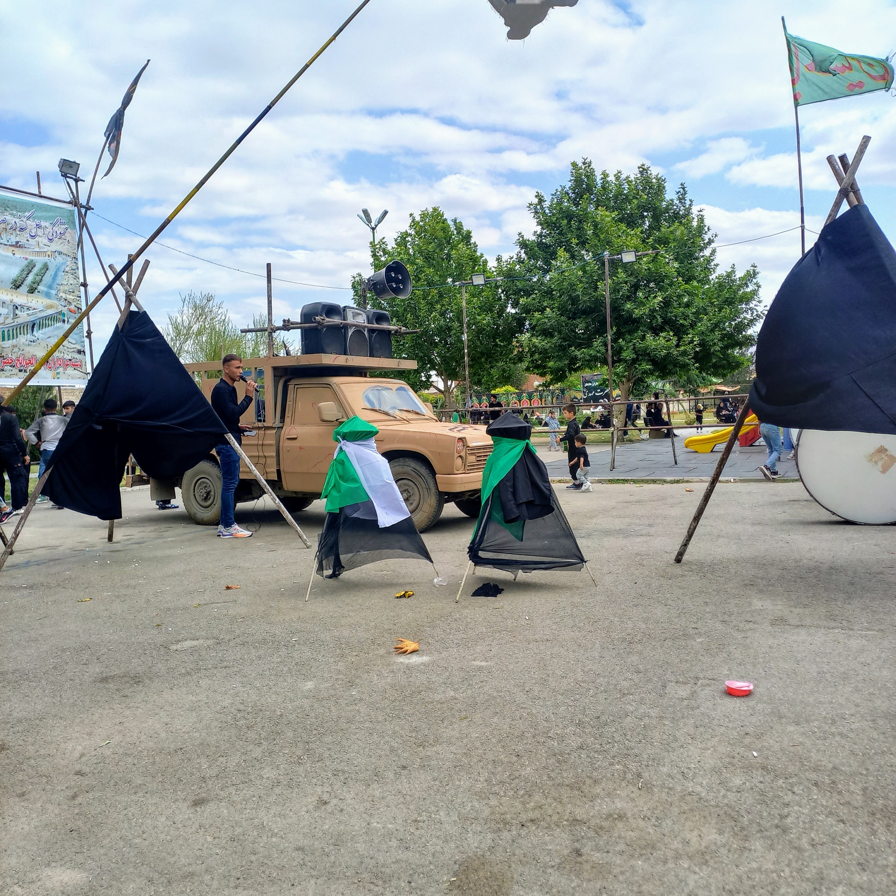 علامت‌های بزرگ سیاه عزا در روز عاشورا بر دوش کودکان سیاه‌پوش سنگینی می‌کند و پرچم سبز بر فراز آن‌ها به اهتزاز درآمده است. وانت بلندگوها نوای روضه را پخش می‌کند و این کودکان معصوم، با تمام وجود، یاد مظلومیت امام حسین (ع) و علمدار کربلا را زنده نگه می‌دارند؛ صحنه‌ای که قلب هر بیننده‌ای را به درد می‌آورد و عشق حسینی را جاودانه می‌سازد.عاشورا حسینی | ۲۶ تیر ۱۴۰۳ | ارومیه، بوستان صفا 🖤 یا عباس (ع)