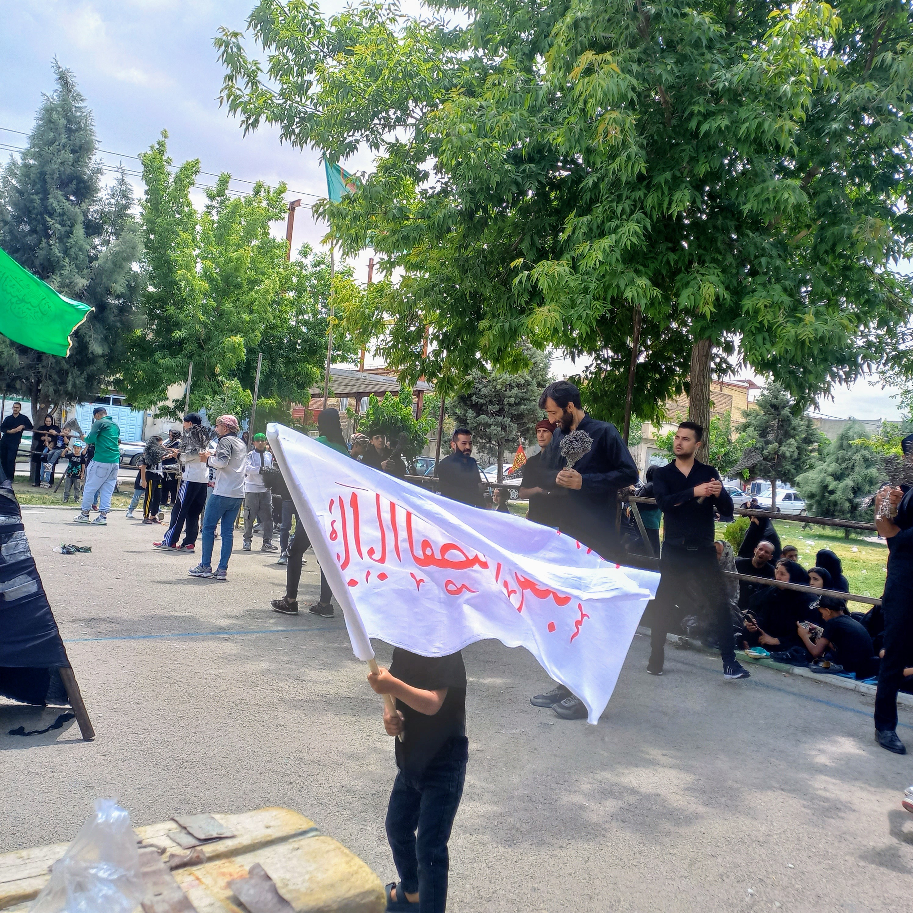 کودکی کوچک با پرچمی سفید و نوشته‌ای سرخ بر دوش، پیشاپیش عزاداران گام برمی‌دارد: «یا ابالفضل العباس ». این تصویر زیبا، نشان می‌دهد که نام حسین (ع) از کودکی بر زبان و دل‌ها جاری است و نسل به نسل، عشق به او منتقل می‌شود.تاسوعای حسینی | ۲۵ تیر ۱۴۰۳ | ارومیه، بوستان صفا 🖤 یا اباعبدالله الحسین