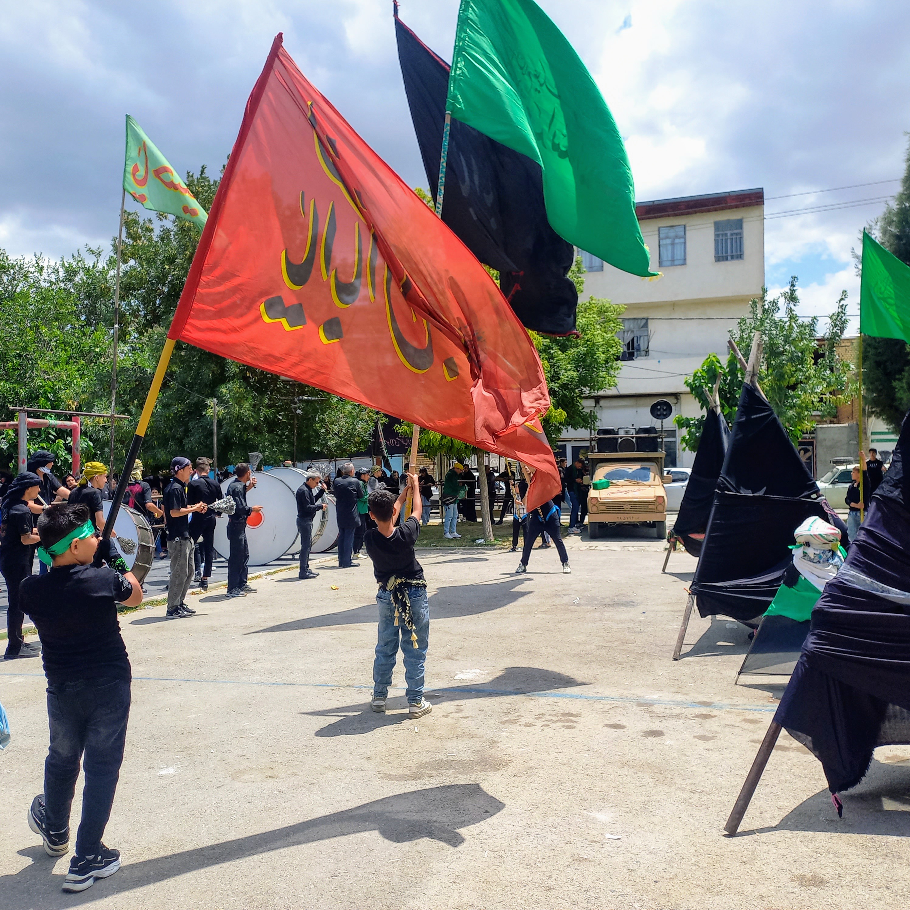 پرچم‌های بزرگ عزا در باد تاسوعا به اهتزاز درآمده‌اند؛ سرخِ «یا ابالفضل العباس » ، سبزِ وفاداری به عباس (ع) و سیاهِ ماتمِ کربلا. کودکی با تمام وجود پرچم سنگین را بر دوش گرفته و طبل و سنج، نوای «حسین حسین» را در آسمان بوستان صفا طنین‌انداز کرده است.تاسوعای حسینی | ۲۵ تیر ۱۴۰۳ | ارومیه، بوستان صفا 🖤 یا لثارات الحسین