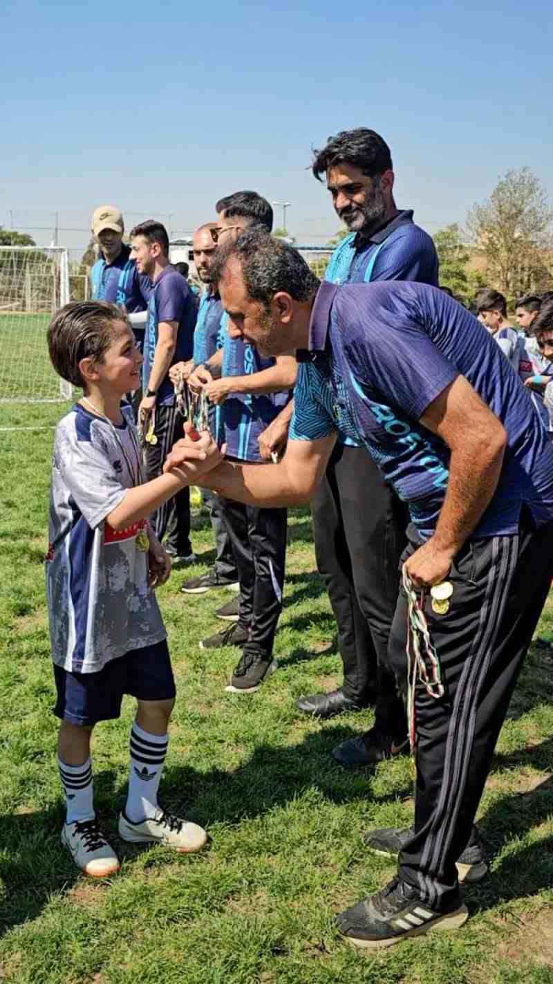 تصویر فوتبالیستهای نونهال بهترین مدرسه فوتبال ،روستوف ایران با لباس طوسی خوشحال در حال گرفتن مدال از مربی خود