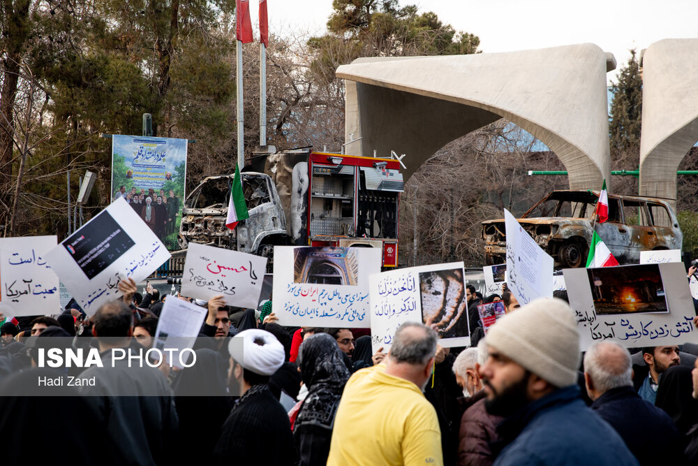 نمایش پلاکاردها توسط مردم و تجهیزات شهری آسیب دیده در مقابل دانشگاه تهران - راهپیمایی همبستگی ملی - تهران 22 دی 1404
